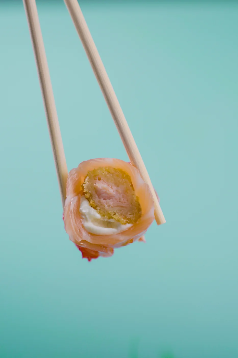 Peça de sushi do Utida Express entre hashis, sobre fundo turquesa